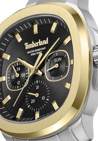 Kvadrāta formas Timberland pulksteņi ar melnu ciparnīcu, zelta akcentiem un sudraba metāla siksniņu. Iekļauj datuma un dienas subdatus, ūdensizturīgs līdz 50m.