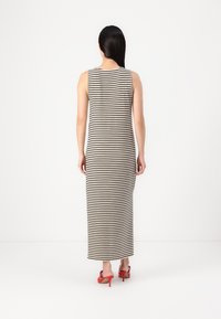 Robe longue sans manches rayée avec une silhouette ajustée, présentant des rayures verticales noires et crème ; portée avec des sandales à talons hauts rouges.