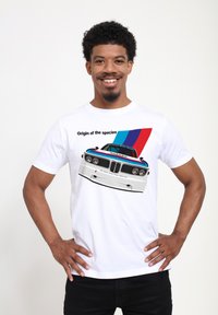 Hvid T-shirt med et grafik af en BMW bil og teksten "Originen af arterne", pyntet med blå og røde diagonale striber.