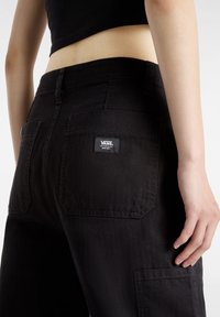 Svarta denim cargo byxor med fickor, en etikett på baksidan, med en slitstark struktur och en något avslappnad passform.