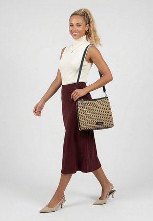 Vrouw met blonde paardenstaart, gekleed in witte mouwloze coltrui en bordeauxrode rok, met een schoudertas met patroon, lopend op beige hakken.