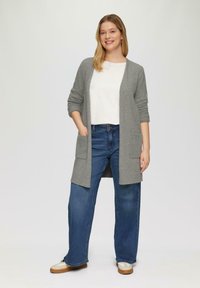 Grijze cardigan met lange mouwen en twee zakken, gedragen over een witte top en blauwe wijde jeans. De cardigan heeft een zachte textuur en een ontspannen pasvorm.