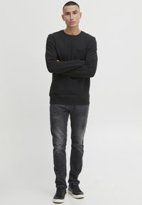 Black sweatshirt with long sleeves and a chest pocket, paired with faded gray jeans and black sneakers. Simple, casual design.