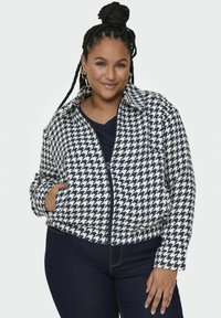 Kurtka w wzór houndstooth w granatowo-białe pasy, z zamkiem błyskawicznym, kołnierzykiem oraz bocznymi kieszeniami. Noszona z granatową bluzką i ciemnymi dżinsami.