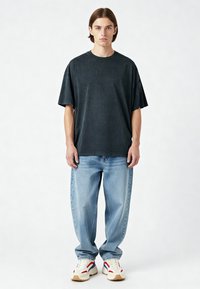 Overmaat zwarte katoenen t-shirt met korte mouwen, gecombineerd met lichtblauwe denim jeans en stevige witte sneakers met rode en blauwe accenten.