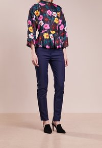 Kwiatowy top z baskinką w żywych różowych, żółtych i białych kwiatach na ciemnym tle; zestawiony z dopasowanymi granatowymi spodniami i czarnymi szpilkami.