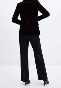 Blazer en velours bordeaux à la coupe cintrée, associé à un pantalon noir à jambes larges et des escarpins à talons aiguilles. Texture lisse et lignes épurées.