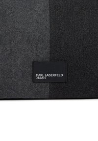 Ciemnoszara tkanina dżinsowa z czarną prostokątną naszywką, na której białymi dużymi literami widnieje napis "KARL LAGERFELD JEANS".