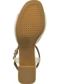 Sandal in pelle bianca con suola in gomma marrone, caratterizzata da una base a motivo e una cinturini con un accento di fibbia color oro. Marchio Geox visibile.