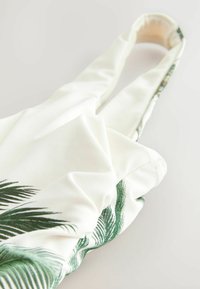Haut en tissu blanc avec des motifs de feuilles de palmier vertes, au toucher lisse et à encolure arrondie. Comprend des bretelles ajustables.