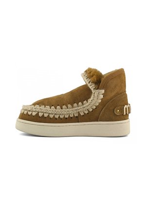 Stivale alla caviglia in suede color sabbia con bordatura intrecciata, fodera morbida, dettagli cuciti, suola piatta color crema e logo in metallo accentato sul tallone.