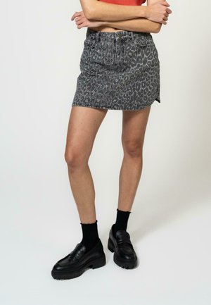 Jupe mini en denim à imprimé léopard gris avec une coupe décontractée, dotée d'une taille avec passants de ceinture et de fentes latérales discrètes. Associée à des mocassins noirs.