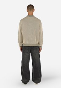 Bežinė raukšlėta megztinė su apvalia iškirpte, derinama su laisvo silueto tamsiai pilkomis kelnėmis, turinčiomis galines kišenes. Lygus, tekstūruotas audinys.