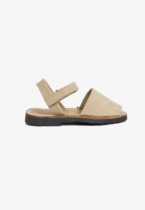 Sandale en cuir beige avec deux sangles réglables, bout ouvert et semelle en caoutchouc noir texturé. Présente des coutures légères le long des bords.