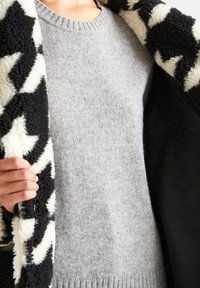 Szary sweter z grubym, dzianym wzorem, noszony pod czarno-białą, futrzaną kurtką w gwiazdkowy wzór. Posiada okrągły dekolt i prążkowany dół.