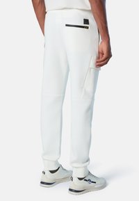 Pantalones de chándal blancos con un diseño elegante, que cuentan con dos bolsillos laterales, un bolsillo con cremallera y puños acanalados. Confeccionados con una tela suave y texturizada.