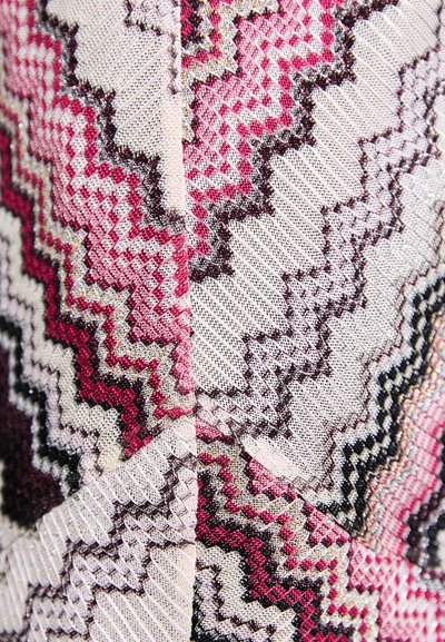 Textiel met een zigzagpatroon in roze, crème en zwarte tinten. De textuur is geweven met metallic accenten, wat diepte en visuele interesse creëert.