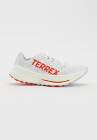 Jasnoszary but sportowy z grubą białą podeszwą i czerwonym logo "TERREX" po boku, zaprojektowany do biegania w terenie lub aktywności na świeżym powietrzu.