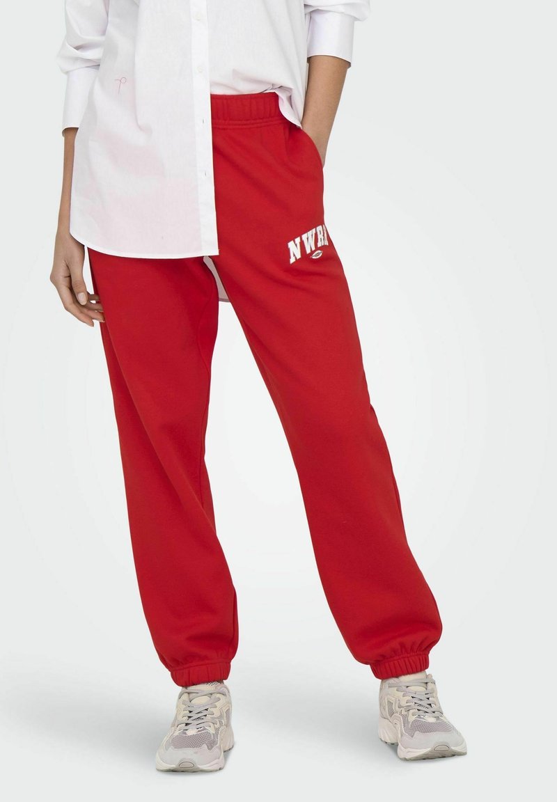 Røde sweatpants med elastisk talje og cuffs, prydet med hvid "NWR" logo. Glat stofstruktur, afslappet pasform, parret med lyse sneakers.