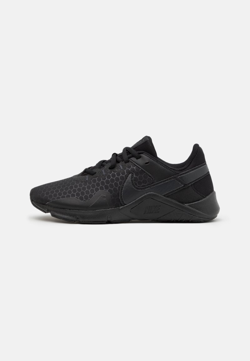 Zapatillas deportivas negras con un patrón hexagonal, superposiciones texturizadas, diseño de cordones y detalles de marca en el lateral y el talón.
