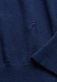 Marineblauwe gebreide trui met een zachte textuur. Voorzien van een klein, geborduurd logo op de borst en geribbelde manchetten en zoom.