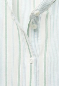 Chemise en tissu blanc avec des rayures verticales bleues et vertes, dotée d'un col et de deux boutons en plastique blanc. Tissage texturé visible.