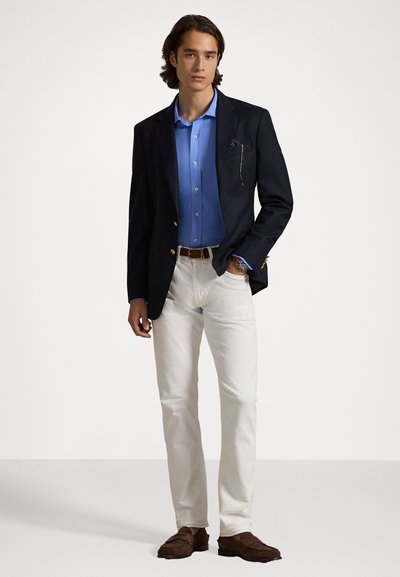 Blazer azul marinho com botões dourados, camisa azul, calças brancas e mocassins castanhos. Inclui um lenço de bolso e tecido texturizado.