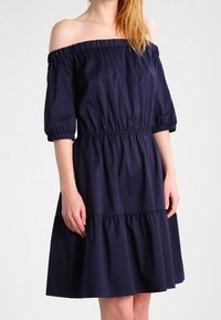 Námornícky šaty s odkrytými ramenami, krátkymi puff rukávmi, elastickým pásom a vrstvenou sukňou. Vyrobené z hladkej, ľahkej látky.
