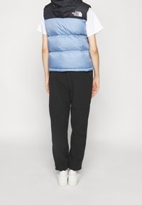 Kamizelka puchowa w jasnoniebieskim i czarnym kolorze, z kapturem i logo. W zestawie luźne czarne spodnie dresowe i białe trampki. Tło jest jednolicie białe.