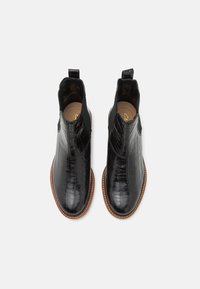 Botas de tobillo de cuero negro con textura de cocodrilo, paneles laterales elásticos, asa en la parte trasera y suela de color marrón claro en contraste.