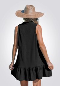 Schwarzes ärmelloses Kleid mit einem gerafften Saum und strukturierter Stoff. Ein breitkrempiger Strohhut vervollständigt das Outfit. Hinteransicht.