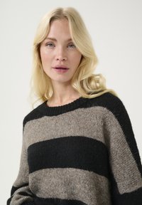 Maglione lavorato a maglia con ampie strisce nere e beige, caratterizzato da un collo rotondo e una texture morbida. Vestibilità rilassata con maniche lunghe.