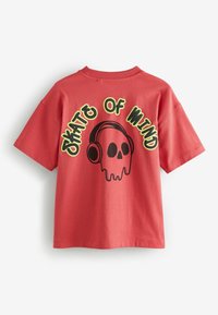 Sarkans kokvilnas T-krekls ar īsām piedurknēm, uz kura ir melna skeleta grafika, kas valkā austiņas, un ap to ir teksts "SKATE OF MIND" dzeltenā krāsā.