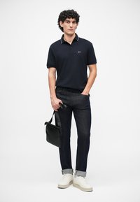 Granatowa koszulka polo z białym kołnierzykiem, ciemnogranatowe dżinsy, białe sneakersy i czarna torba na ramię. Prosty design z dopasowanym krojem.