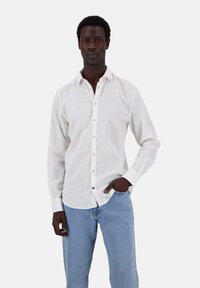 Weißes Hemd mit Knopfleiste aus leichtem Stoff, mit klassischem Kragen und kontrastierenden Knopfakzenten. Kombiniert mit hellblauen Jeans.