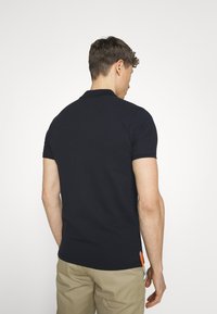 Granatowa koszulka polo wykonana z bawełny, z klasycznym kołnierzykiem i krótkimi rękawami, z małą pomarańczową metką u dołu.