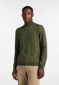 Maglione verde a collo alto realizzato in tessuto maglia, con un design aderente, polsini a coste e un logo discreto sul petto.
