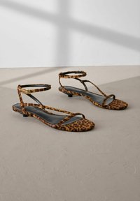 Flat sandaler i leopardmönster med svarta läderinlägg, med tunna ankelremmar och en minimalistisk design. Texturerat mjukt tyg.