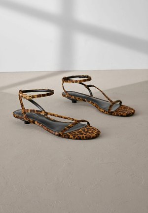 Leparda raksta plakanās sandales ar melniem ādas iebūvētajiem zolēm, tām ir plānas potītes siksniņas un minimālisma dizains. Tekstūrēts mīksts audums.