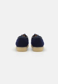Sapatos em azul-marinho com um upper em tecido texturizado, detalhes em couro liso e uma sola de borracha em tom claro; apresenta um perfil baixo e uma forma arredondada.