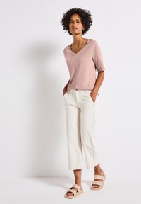 T-shirt a scollo a V rosa chiaro, maniche corte, abbinata a pantaloni larghi color crema e sandali beige con tacco a scivolo. Tessuto morbido, design casual.