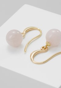 Auksinės spalvos kabantys auskarai, pagaminti su apvaliais, šviesiai rožiniais kvarco karoliukais su lygiu paviršiumi, elegantiška kreive ir minimalistiniu dizainu.