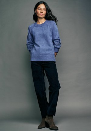 Blå strikket sweater med ribbede manchetter og kant, parret med mørke denimbukser og brune suedeboots til anklen. Simpelt design, blød tekstur.