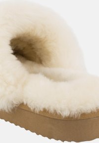 Crème-kleurige slipper met een pluche, fluffy voering en een duurzame, textuurgegeven zool. Heeft een zachte, wolachtige bovenkant.