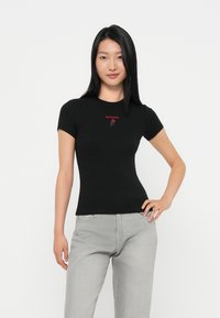 Crna priljubljena majica s kratkim rukavima, s crvenim natpisom "tommy jeans" i grafikom ruže. Glatka tkanina s okruglim izrezom. Uparena s svijetlosivim trapericama.