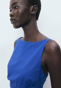 Robe sans manches en tissu bleu vif avec une texture lisse. Dotée d'un décolleté bateau, d'un buste ajusté et d'une silhouette structurée.