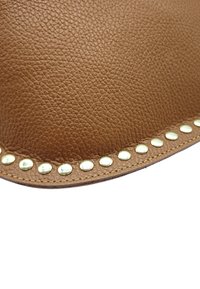 Cuir texturé marron avec des rivets dorés le long du bord, comportant une couture. La surface présente des motifs de grain naturel.