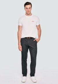 Balta trumpa rankovėmis marškiniai su raudonu užrašu "merry." derinami su pilkai languotomis kelnėmis ir baltais sportbačiais. Rudas diržas pabrėžia liemenį.