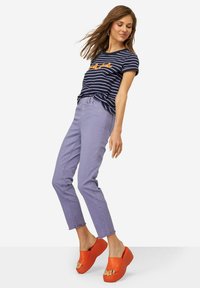 Camiseta a rayas azul marino con texto naranja, combinada con pantalones de tobillo de color púrpura claro y sandalias de plataforma naranjas. Tejido suave, ajuste casual.