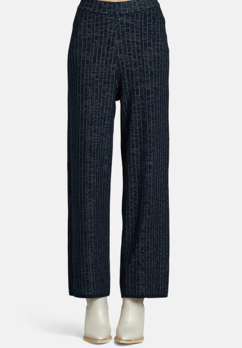 Högmidjade, vida mörkblå byxor med subtil vertikal randning, kombinerade med vita ankelstövlar på en enfärgad bakgrund.